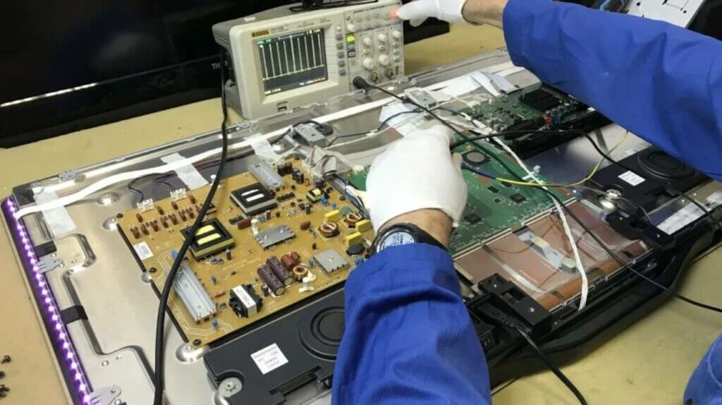 A mechanic repairing the audio section of a TV, using tools to adjust and fix electronic components on the circuit board.