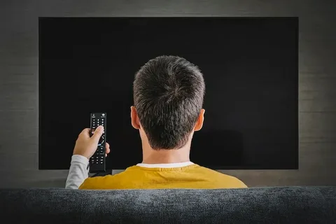 A person viewing a completely black TV screen, symbolizing a TV that is not turning on or is experiencing an electrical failure due to power surges or faulty internal components.